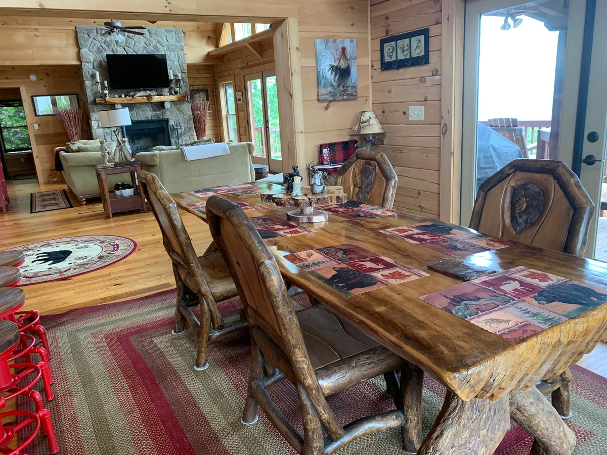 A large wooden dining table set by a stone fireplace, with a comfortable seating area and expansive windows framing the mountain views. The space exudes warmth and provides a seamless transition between dining, lounging, and soaking in the scenery.