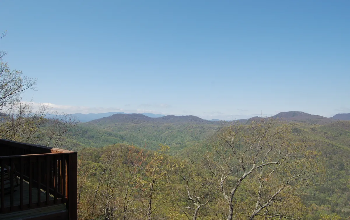 A sweeping view of a mountain range framed by lush greenery and a clear blue sky, with the vantage point suggesting this could be the scenery visible from the cabin’s deck. The landscape conveys the grandeur and tranquility of the natural surroundings, inviting outdoor exploration and connection to the environment.
