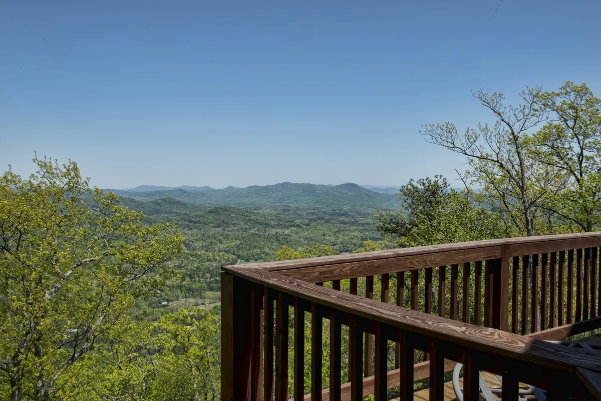 A stretch of deck with a sturdy wooden railing, opening out to a vast landscape of mountains and greenery. The view implies the deck’s wraparound nature and its promise of uninterrupted scenic outlooks from various vantage points.