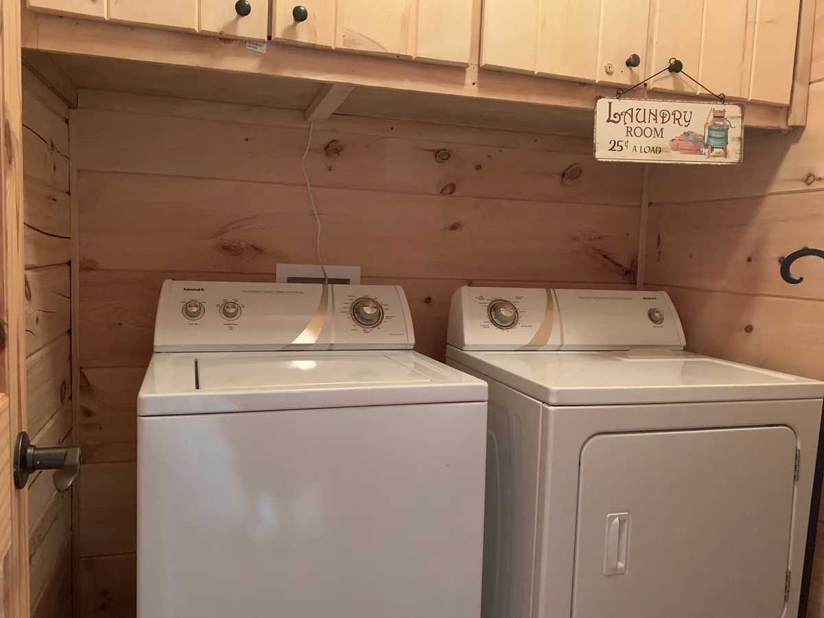A practical laundry area equipped with a washing machine, dryer, wooden cabinetry for storage, and a cheerful laundry sign above. The space is clean, organized, and ready for everyday use.