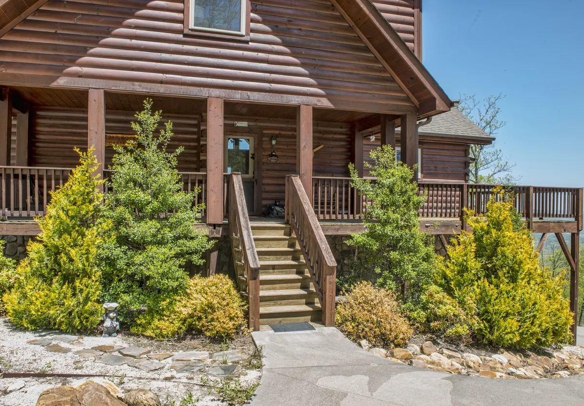 An inviting perspective on the cabin’s wooden stairs, spacious porch, and surrounding greenery. The scene hints at group arrivals, evening conversations, or morning coffees enjoyed in a communal setting with mountain air.