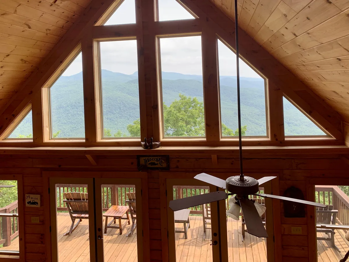 This image features large windows overlooking the mountains, a wooden deck with comfortable seating, and a warm, sunlit atmosphere. The seamless flow between the indoor living space and the spacious outdoor deck invites both relaxation and engagement with nature.